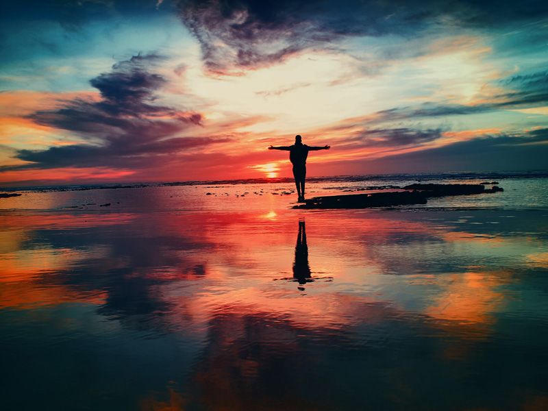 Person with outstretched arms at sunrise
